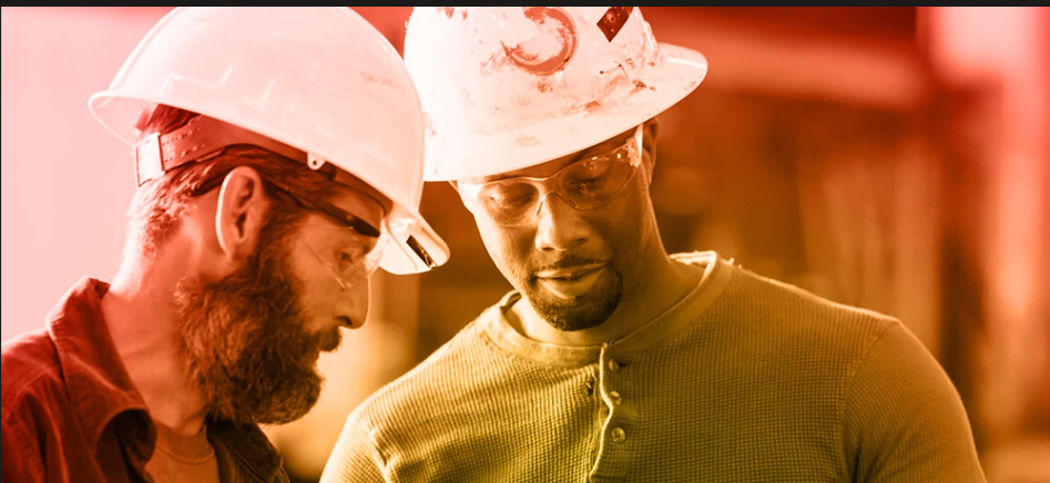 Two construction workers in hard hats reviewing plans together